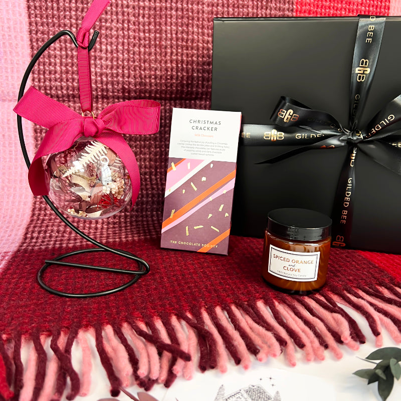 Gift set with Christmas cracker, ornament, and candle on a red blanket