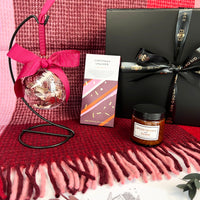 Gift set with Christmas cracker, ornament, and candle on a red blanket