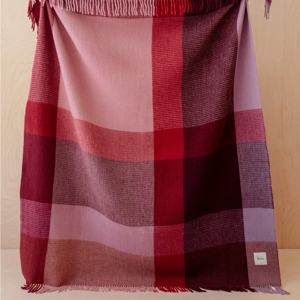 Plaid blanket with red and pink colors draped over a surface against a beige background