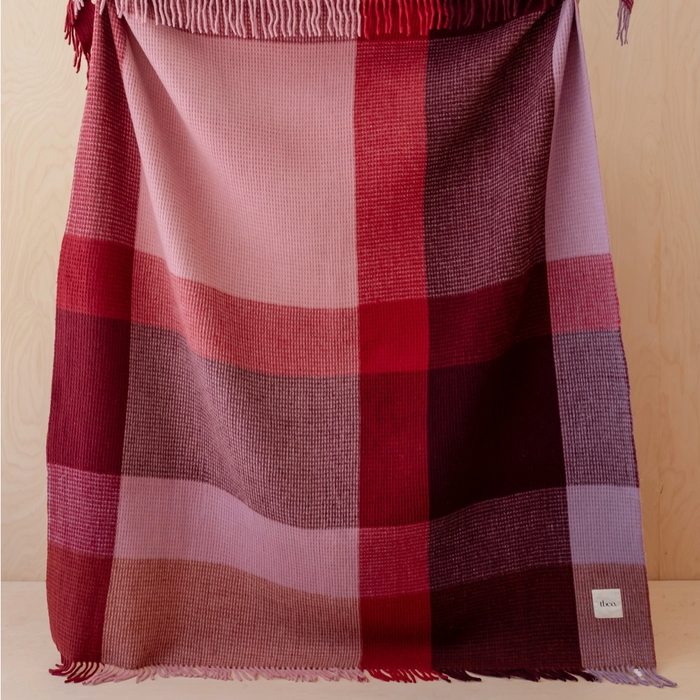 Plaid blanket with red and pink colors draped over a surface against a beige background