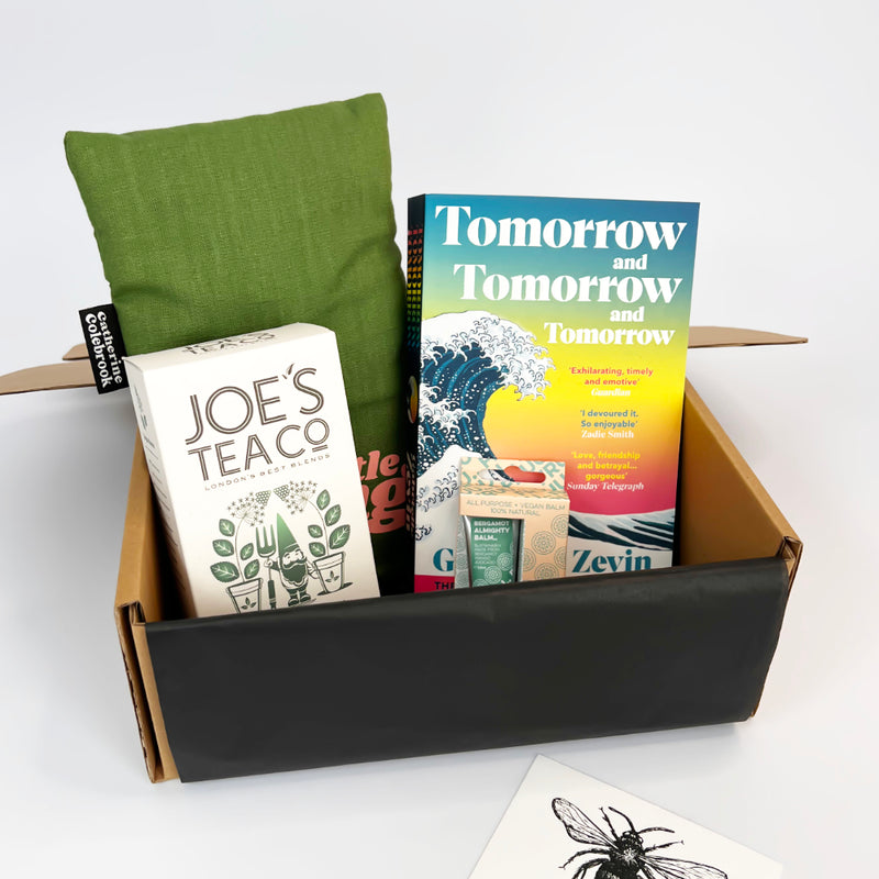Box with books and a green hot water bottle pillow on a white background
