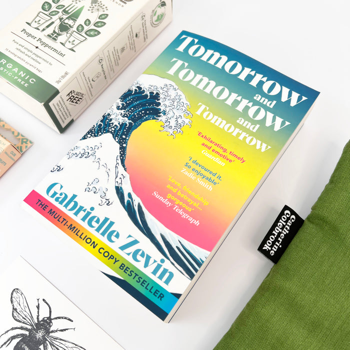 Book titled 'Tomorrow and Tomorrow and Tomorrow' by Gabrielle Zevin on a white surface with a green fabric and other books in the background.