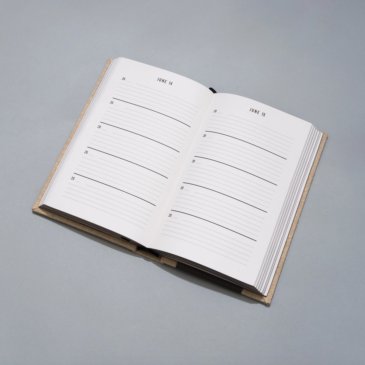 An open hardcover planner or journal with lined daily writing pages, photographed on a smooth light gray surface.