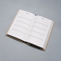 An open hardcover planner or journal with lined daily writing pages, photographed on a smooth light gray surface.