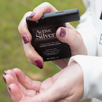 A person holding an Active Silver hand steriliser bottle over their hands, with a blurred outdoor background.