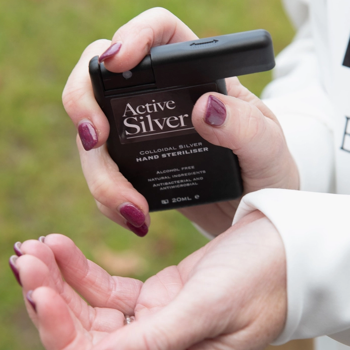 A person holding an Active Silver hand steriliser bottle over their hands, with a blurred outdoor background.