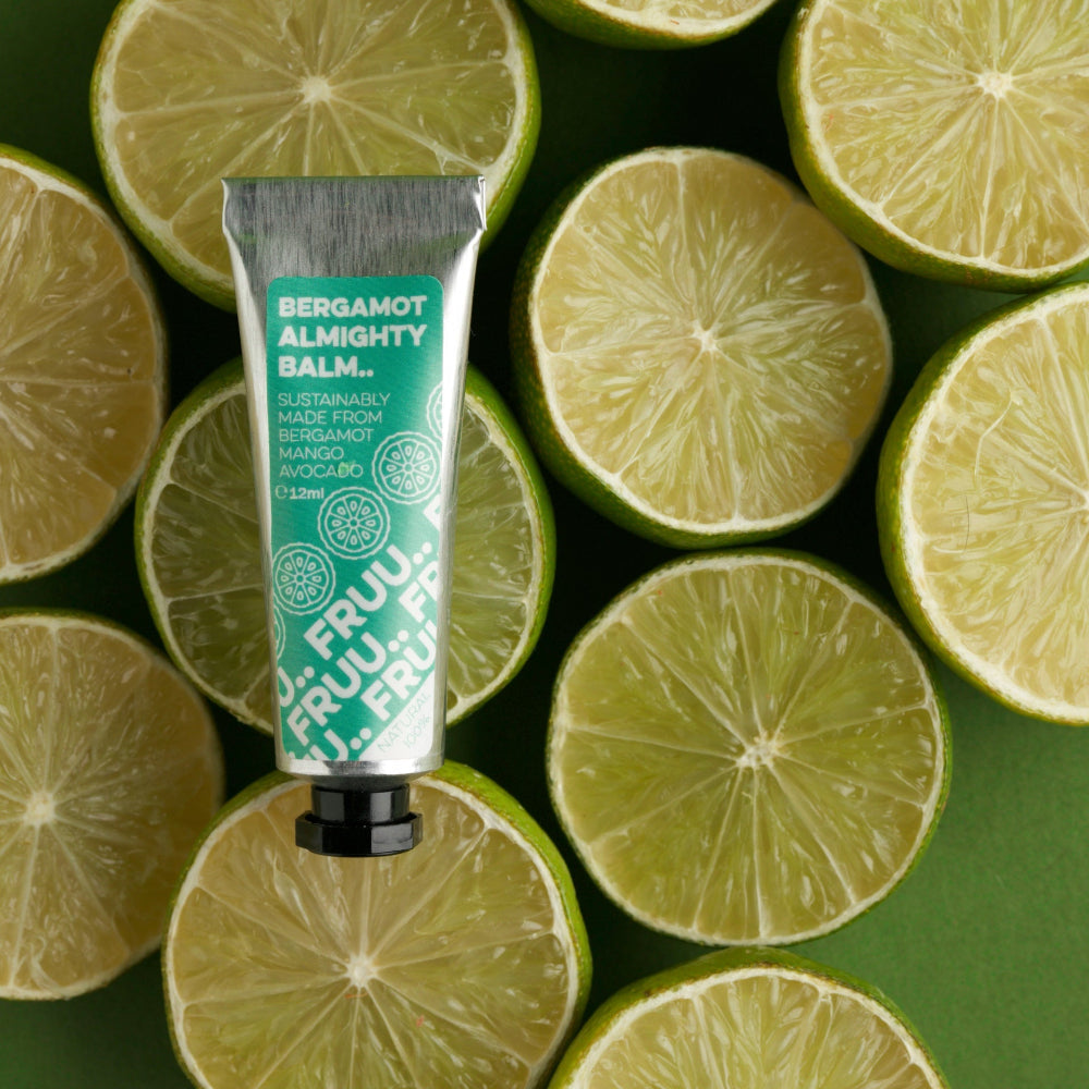 A tube of Bergamot Almighty Balm by Fruu positioned against a background of lime slices.