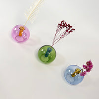 Three small glass wall vases in pastel colors with dried flowers on a white background