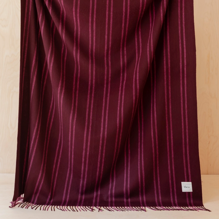 Burgundy Lambs wool blanket with lighter stripes being held up