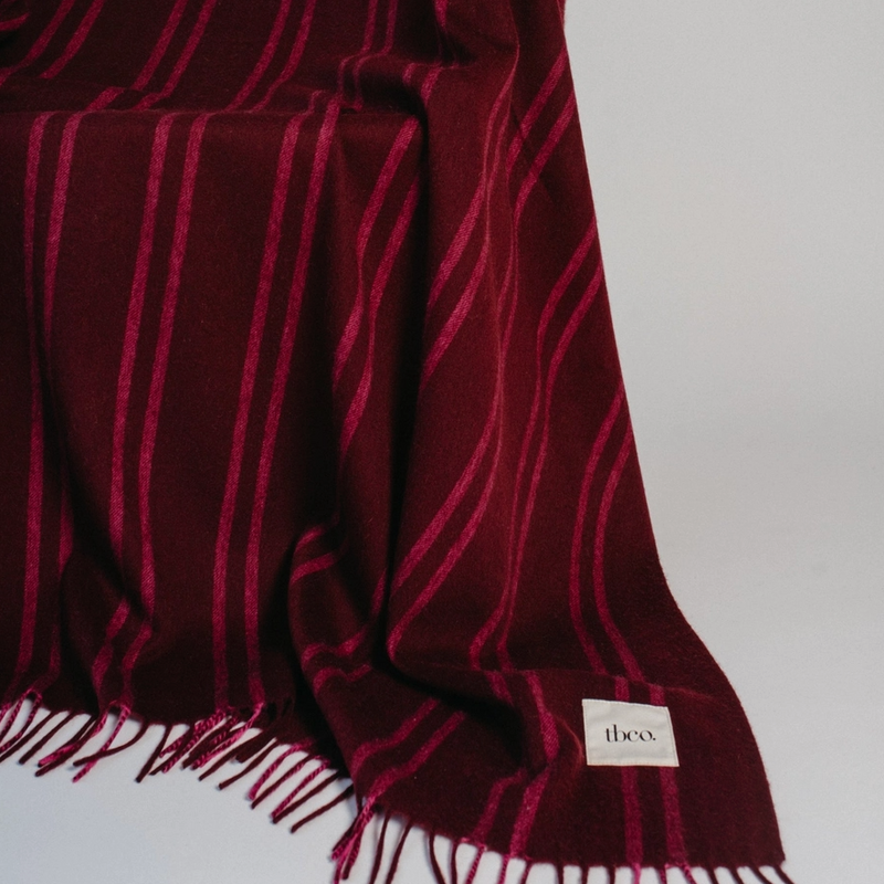 Burgundy and wine striped blanket with fringes on a white background
