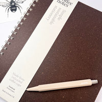 Spiral-bound notebook with a pen on a white background and bee gift card