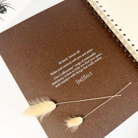 Brown notebook with text and decorative grasses on a white background
