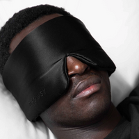 Person wearing a black sleep mask with 'Drowsy' branding on a white background