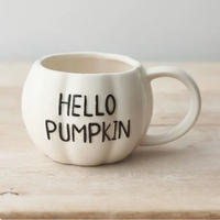 An off-white ceramic mug shaped like a pumpkin with the words 'HELLO PUMPKIN' printed in black on the front, resting on a light wooden surface.