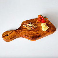 An olive wood serving board with a handle, styled with cherry tomatoes, nuts, and cheese on a clean white background.