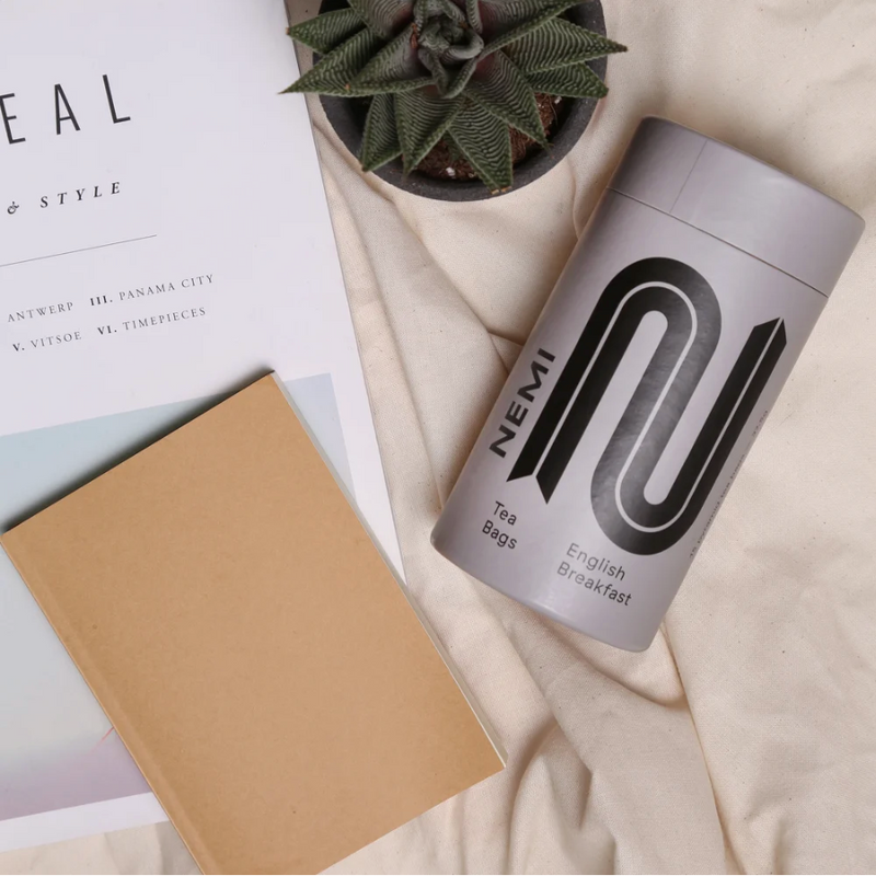 Nemi tea bags container with a notebook and plant on a light surface