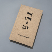 A square-shaped beige linen-bound memory book titled 'ONE LINE A DAY' with black text, photographed on a neutral gray background.