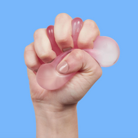 A hand gripping a translucent pink silicone stress ball against a solid blue background.