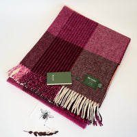 A woven plaid scarf in shades of magenta, burgundy, and brown, with cream fringe and two green Bronte tags, displayed on a white background.