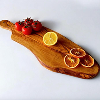 A rustic wooden serving board with a live edge, styled with cherry tomatoes on the vine and dried orange slices, set against a plain light gray background.