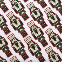 A repeating pattern of nutcracker-shaped items on a white background, each featuring a cream face and torso with dark green and red clothing details, yellow geometric accents, and a black beard.