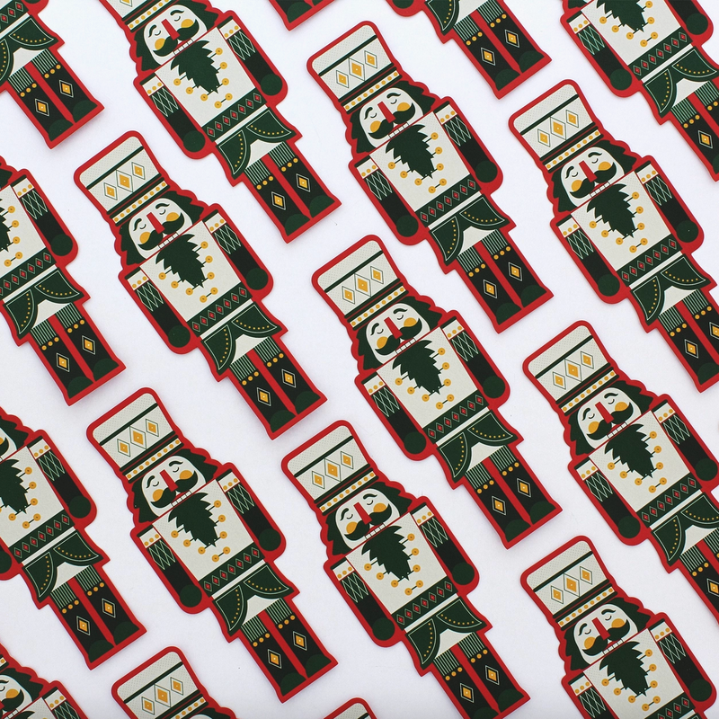 A repeating pattern of nutcracker-shaped items on a white background, each featuring a cream face and torso with dark green and red clothing details, yellow geometric accents, and a black beard.