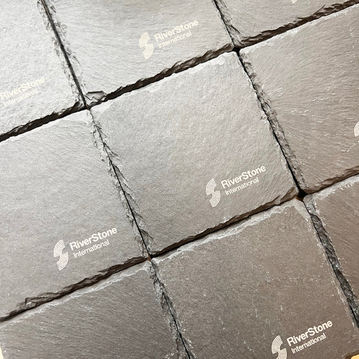 Grey slate coaster arranged in a grid pattern, showing a textured stone surface with visible RiverStone International watermarks.