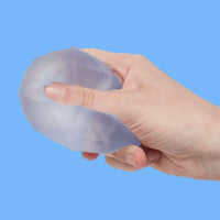 Hand holding a silicone breast implant against a blue background
