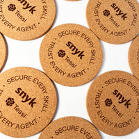 Cork coasters with 'snyk' and 'Tessi' branding on a white background