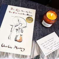 The boy, the mole, the fox and the horse book on a navy blanket with lit candle