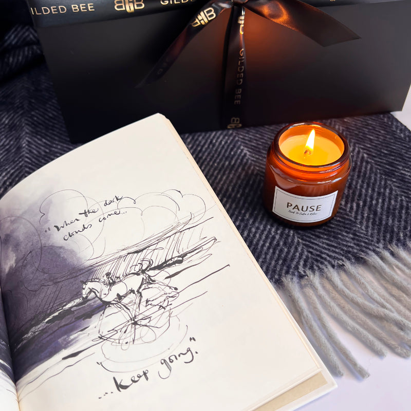 Candle labeled 'Pause' next to an open book with illustrations on a textured surface