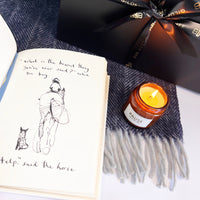 Book open with a quote about asking for help and lit Pause candle with Gilded bee luxury gift bow behind.