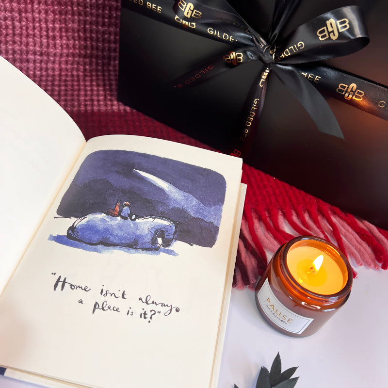 Quote 'home isn't always a place is it" book open with pause candle and gilded bee gift box