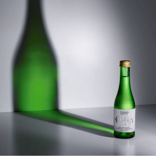 Green bottle with gold cap on a gray surface with a gray background