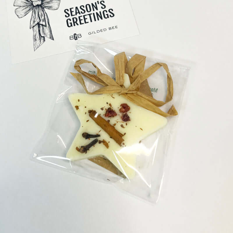 Star-shaped white chocolate candy with cinnamon sticks and raisins in a clear bag, branded 'Gilded Bee'.