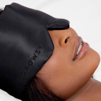 Person wearing a black sleep mask with 'Drowsy' branding on a white background